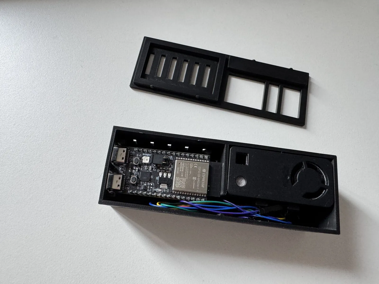 The finished enclosure, open: the board clipped into the left chamber with both USB sockets in their windows, the sensor in the right chamber, cables running through the divider wall, and the lid lying next to it